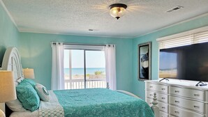 A bedroom with a bed, a dresser, a television, and a window with a view of the beach. - Oceanfront House, Screen Porch, Boardwalk, Volleyball Sand Court, Game Room (Pawleys Island)