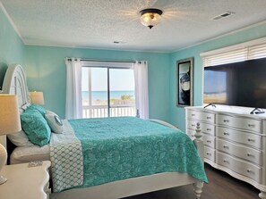Quarto com cama, penteadeira, televisão e janela com vista para a praia.