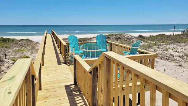 A wooden boardwalk leading to beach chairs and a table, with a clear view of the ocean. - Oceanfront House, Screen Porch, Boardwalk, Volleyball Sand Court, Game Room (Pawleys Island)