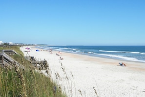 Ein Strand mit einer Holzpromenade, Zelten und entspannten Menschen.