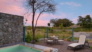 Un muro de piedra, un jacuzzi, una mesa con sillas y una tumbona en un jardín.