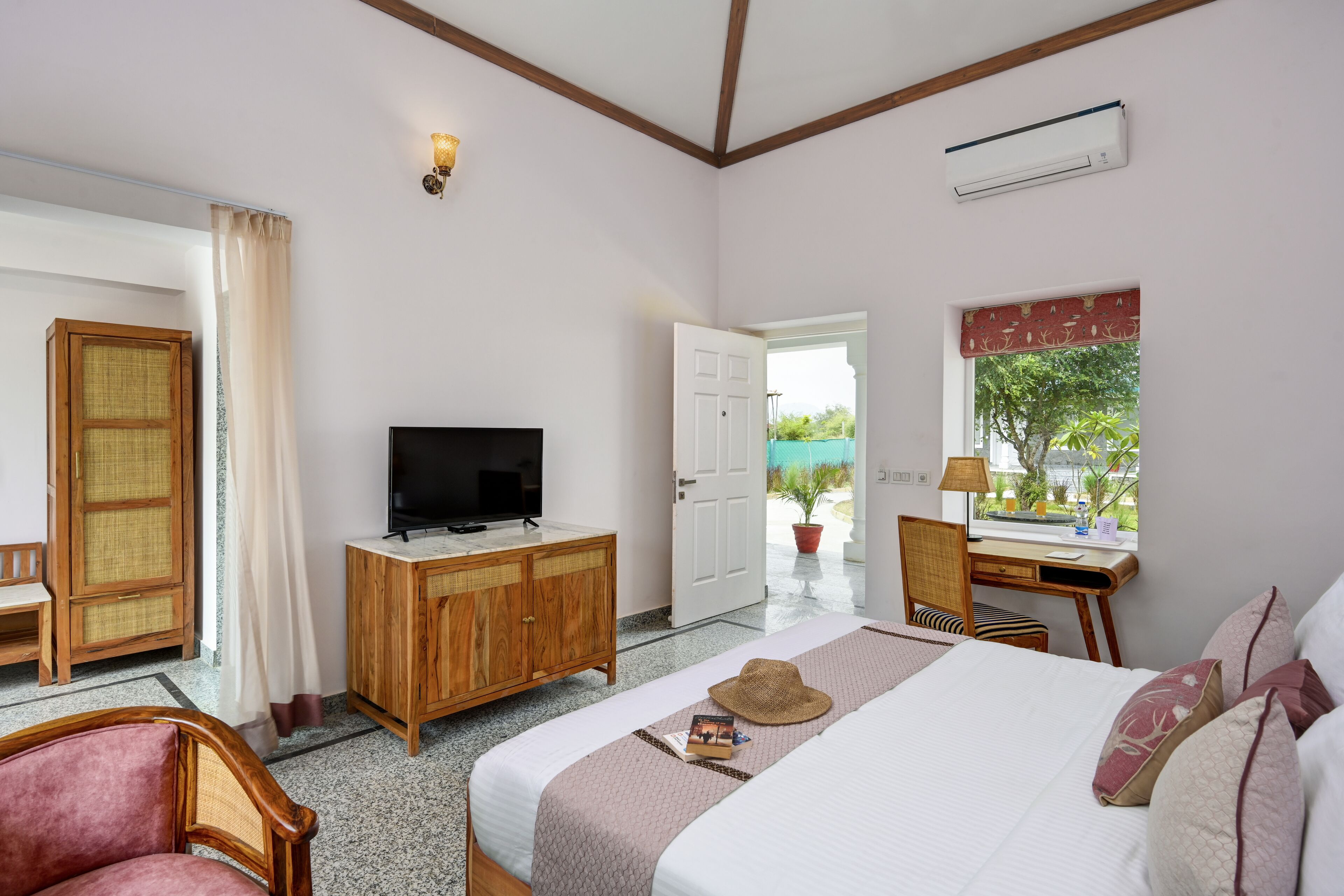 Une chambre d’hôtel comprenant un lit, une télévision, une armoire en bois, un bureau et une fenêtre donnant sur un paysage verdoyant.