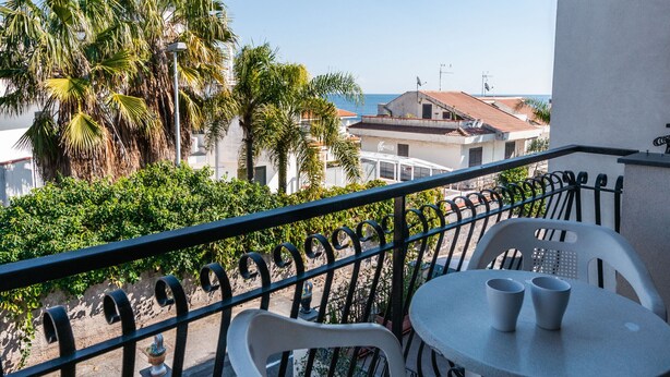 En balkon med et bord og stole, der ud til et kystområde med palmer og bygninger.