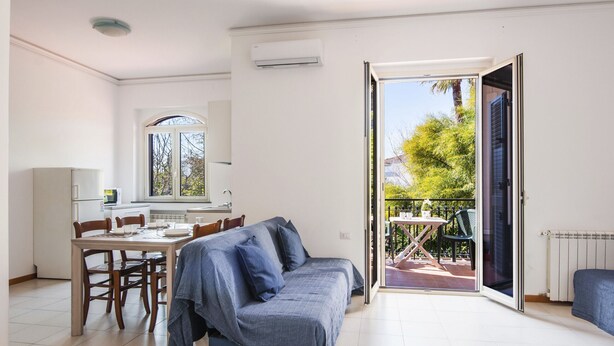 A modern living room with a sofa, dining table, chairs, and a sliding glass door leading to an outdoor patio.