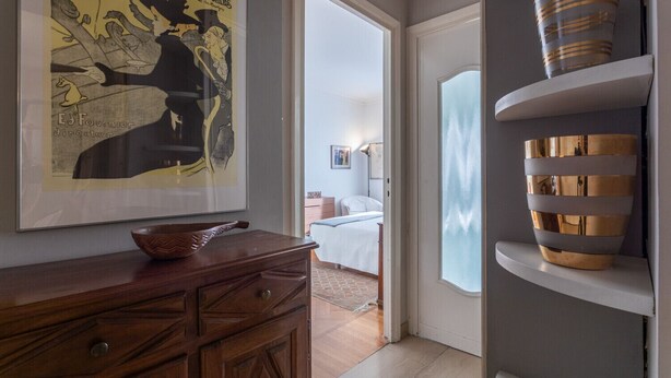 Un couloir avec une commode en bois, une affiche encadrée et une étagère moderne agrémentée d’objets décoratifs.