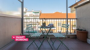 Un balcon avec une table et des chaises, un pot de fleurs et une vue sur les bâtiments.