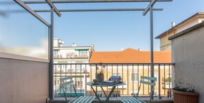 Un balcon avec une table et des chaises, un pot de fleurs et une vue sur les bâtiments.