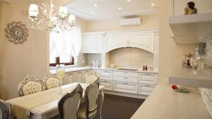 A dining area with a white table and chairs, a chandelier, and a kitchen with white cabinets and a built-in oven. - Luxury Vale Villa. (Locorotondo)