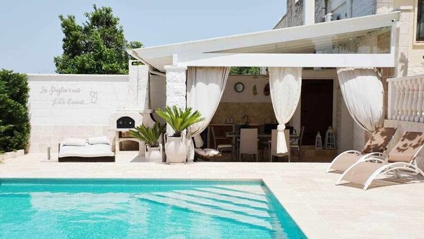 A poolside area with a pool, lounge chairs, a bed, and a dining area. - Luxury Vale Villa. (Locorotondo)