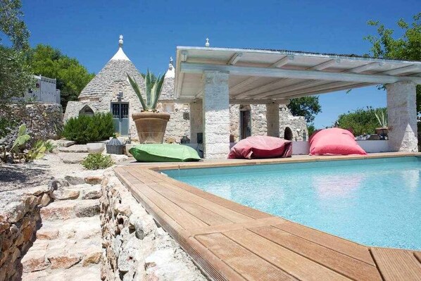 A pool area with a stone building, a covered seating area, and a wooden deck.