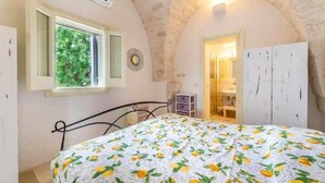 Quarto com cama, janela com vista para área verde, guarda-roupa e porta que dá para outro cômodo.