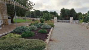 Uma entrada portão com muro de pedra e portão metálico, acessível por um caminho de cascalho.