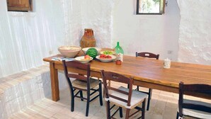 Un comedor rústico con una mesa y sillas de madera, rodeado de paredes blancas y un ventanal pequeño.