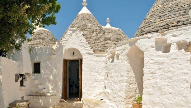 Un edificio de piedra tradicional con un acceso central, escalones de piedra que lo conducen y una pequeña planta en maceta en un alféizar.