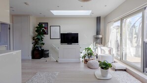Una sala de estar moderna con un televisor de pantalla plana, ventanas amplias y una escalera que sube a otro nivel.