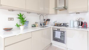 Cocina moderna con armarios blancos, campana extractora de acero inoxidable, horno Bosch y cafetera.