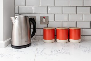 A stainless steel kettle, two red containers, and a light switch on a tiled wall.