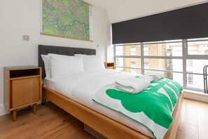 A modern bedroom with a large bed, wooden nightstands, a map on the wall, and a view of buildings through a large window.
