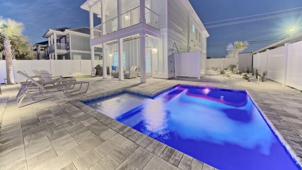 A modern house with a swimming pool, outdoor furniture, and a well-lit patio area.