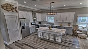 A modern kitchen with white cabinets, a stainless steel refrigerator, a large island with bar stools, and a decorative fish wall art piece.