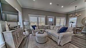 A spacious living room with a sectional sofa, ottoman, and a dining area with a chandelier.