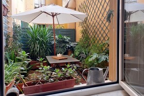 Une petite terrasse avec une table, des chaises, un parasol et diverses plantes en pot.