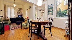 A living room with a round table, chairs, a sofa, a bookshelf, and a window with plants. - Laterano - Apartment for 4 pax with outdoor space close to the Coloseum (Roma)