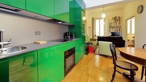 A modern kitchen with green cabinets, a dining area with a wooden table and chairs, a sofa, and a bookshelf. - Laterano - Apartment for 4 pax with outdoor space close to the Coloseum (Roma)