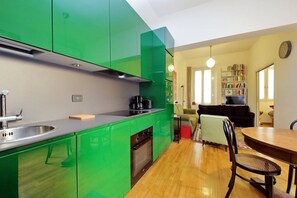 Une cuisine moderne avec des meubles de couleur verte, un coin repas avec une table et des chaises en bois, un canapé et une bibliothèque.