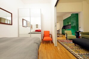 Une pièce comprenant un lit, une chaise, un canapé, un miroir et un coin cuisine vert.