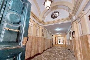 A hallway with a patterned carpet, a large circular ceiling decoration, and a blue door with a brass handle.