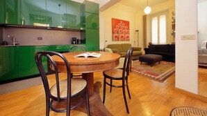 A modern kitchen with green cabinets, a dining table with chairs, a sofa, and a painting on the wall. - Laterano - Apartment for 4 pax with outdoor space close to the Coloseum (Roma)