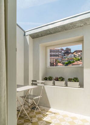 A balcony with a view of historic buildings, a small table, a chair, and potted plants. - Mouzinho 160 (Porto)
