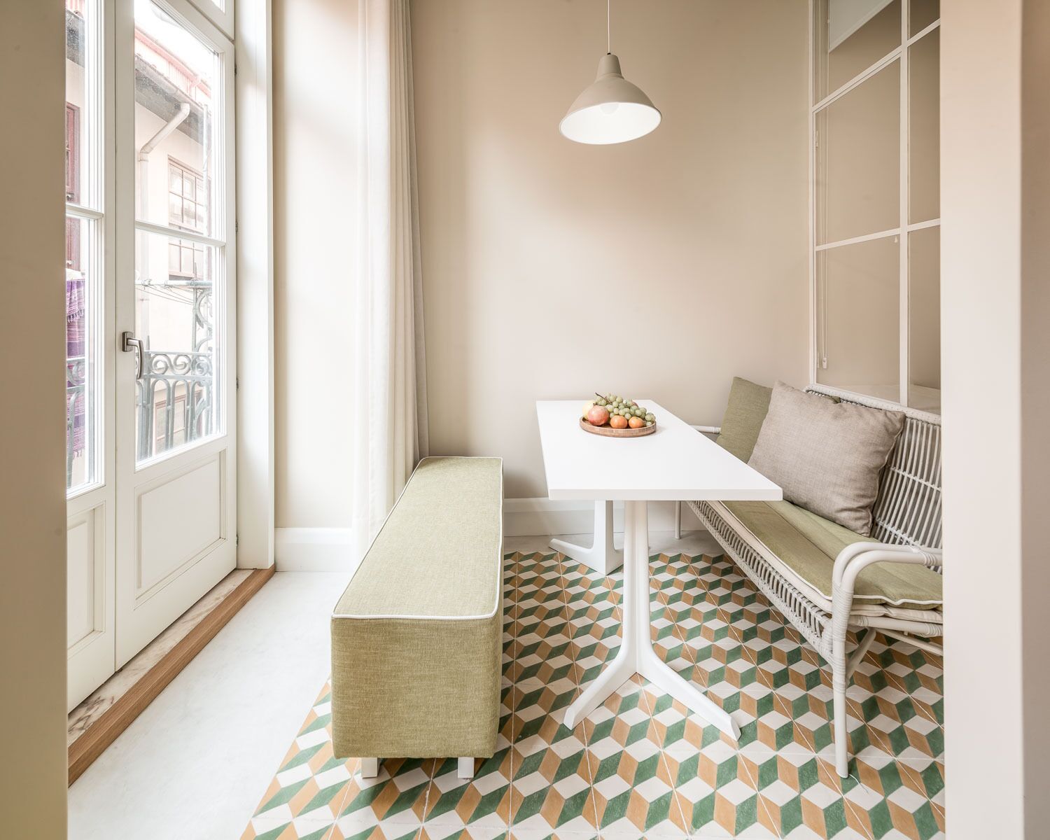 A corner room with a white bench, a small table with fruit, a hanging light, and patterned floor tiles.