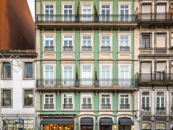 A multi-story building with a green facade, multiple balconies, and storefronts at the ground level. - Mouzinho 160 (Porto)