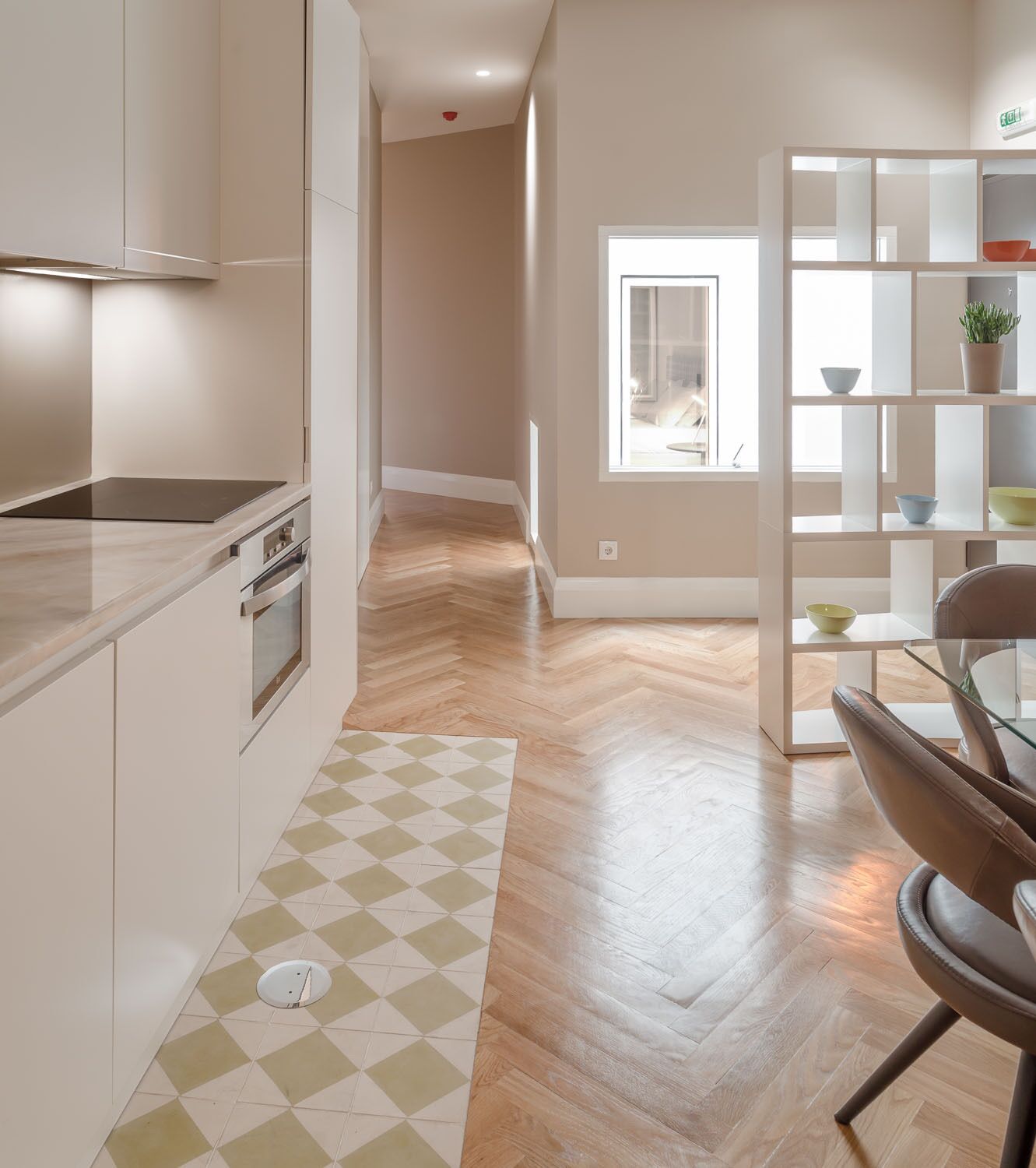 A modern kitchen with a herringbone floor pattern, a built-in oven, and a window overlooking the interior.