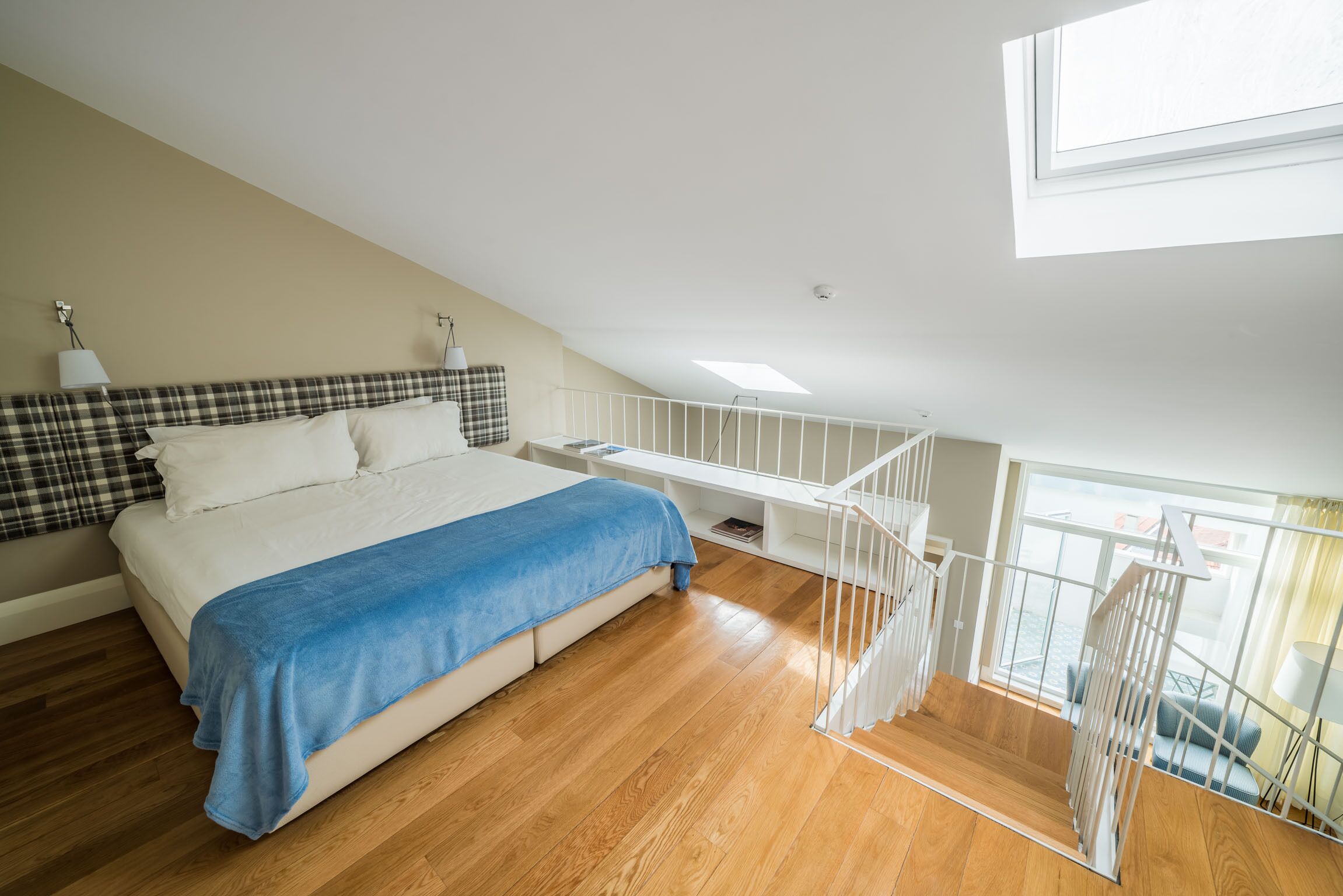 Une chambre à coucher avec un lit, une couverture bleue, un plancher en bois, une balustrade blanche et une fenêtre.