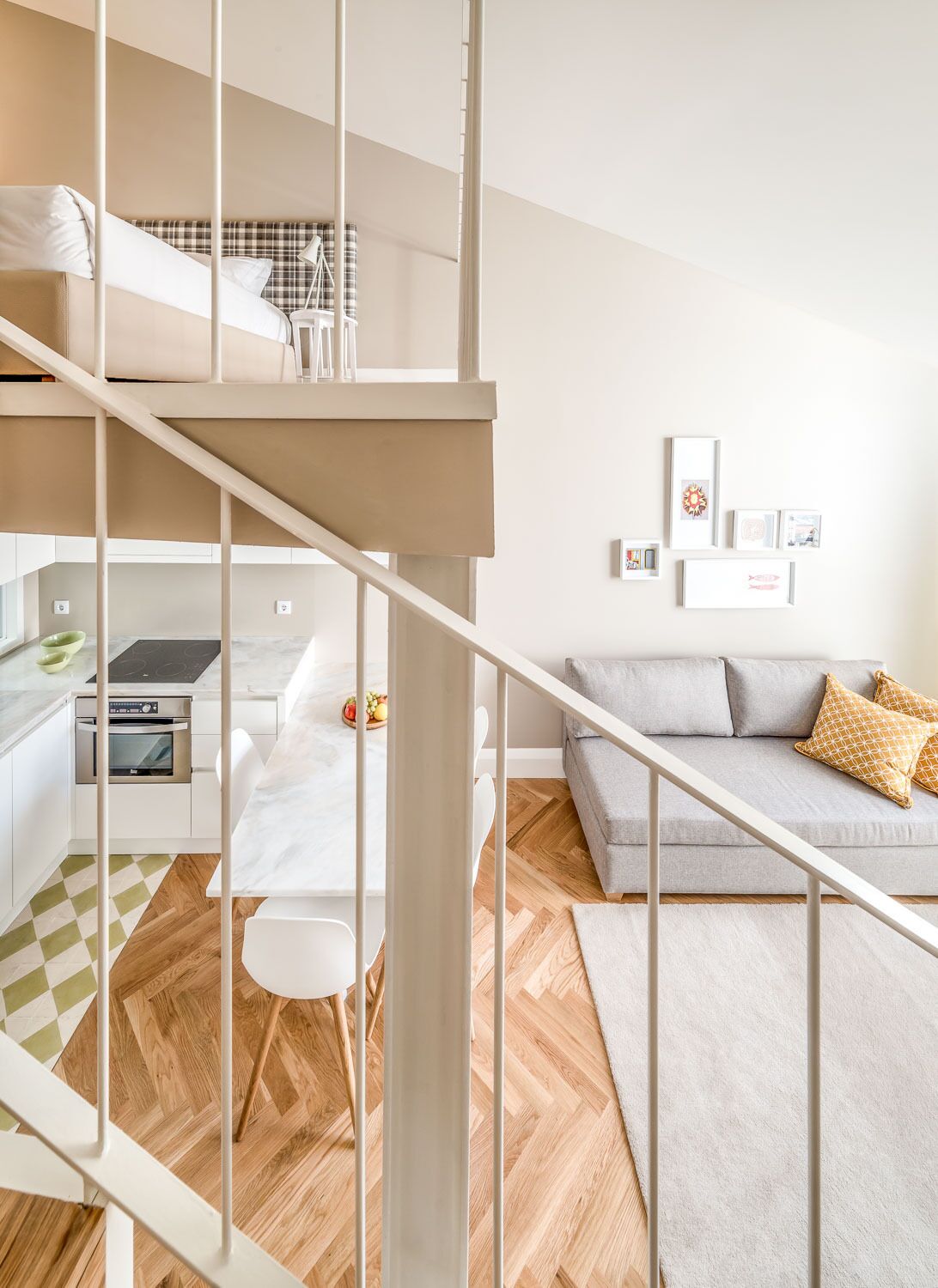 A modern apartment with a staircase leading to a loft bedroom, a kitchen with an oven, a dining area, and a living room with a sofa and cushions.