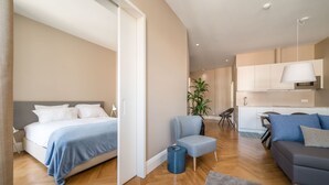 Une chambre d’hôtel moderne comprenant un lit, un coin salon avec un canapé et un fauteuil, une petite table et une plante en pot.