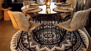 Un comedor con una mesa redonda, seis sillas, un jarrón central y lámparas colgantes.