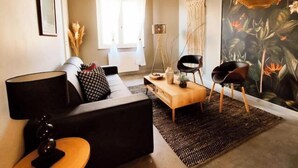 Una sala de estar moderna con un sofá, una mesa de centro y dos sillas. Cuenta con un ventanal con cortinas, una lámpara de pared y un alfombra con textura.