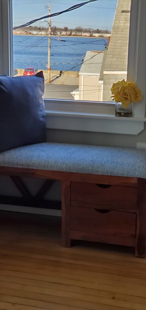 A room with a window seat, a small wooden bench, and a vase with yellow flowers.