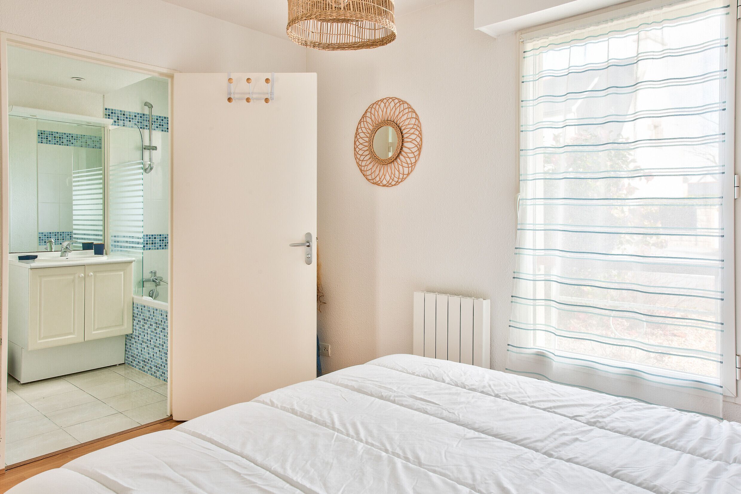 A bedroom with a large bed, a bathroom with a shower, and a view through a window with blinds.