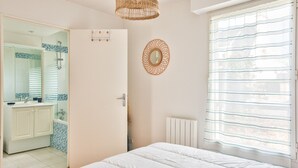 Ein Schlafzimmer mit einem großen Bett, einem Badezimmer mit Dusche und Blick durch ein Fenster mit Jalousien.