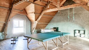 Een ruime zolderkamer met een tafeltennistafel, houten balken en een groot raam.