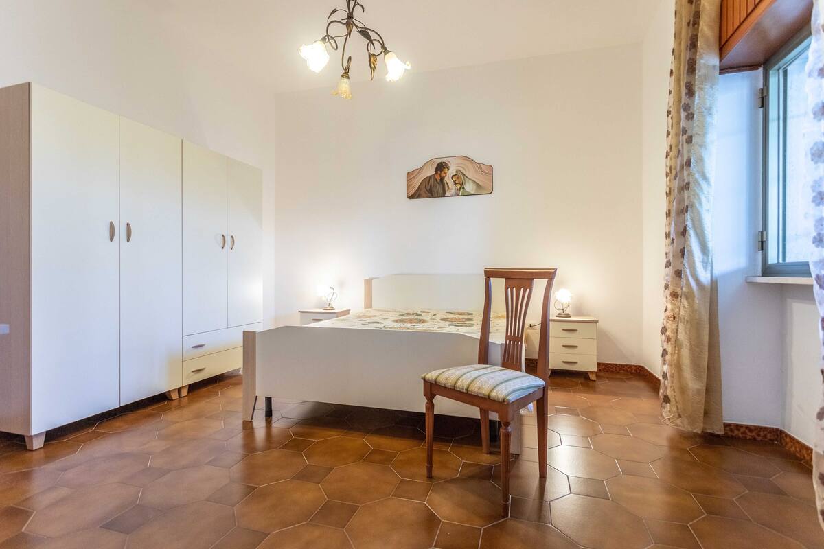 A bedroom with a bed, a chair, a wardrobe, a bedside table, and a nightstand.