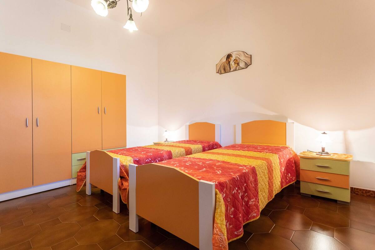 A bedroom with two beds, a wardrobe, a bedside table, and a wall-mounted artwork.