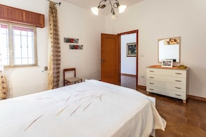 A bedroom with a bed, a dresser, a chair, and a door leading to another room.