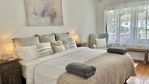 A neatly arranged bedroom with a large bed, bedside tables, a chair, and a window with a view of the outside. - The Ultimate Family Friendly Getaway (Long Jetty)