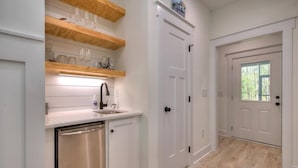 Cucina con mobili bianchi, lavastoviglie in acciaio inossidabile ed mensole in legno sopra il piano di lavoro.